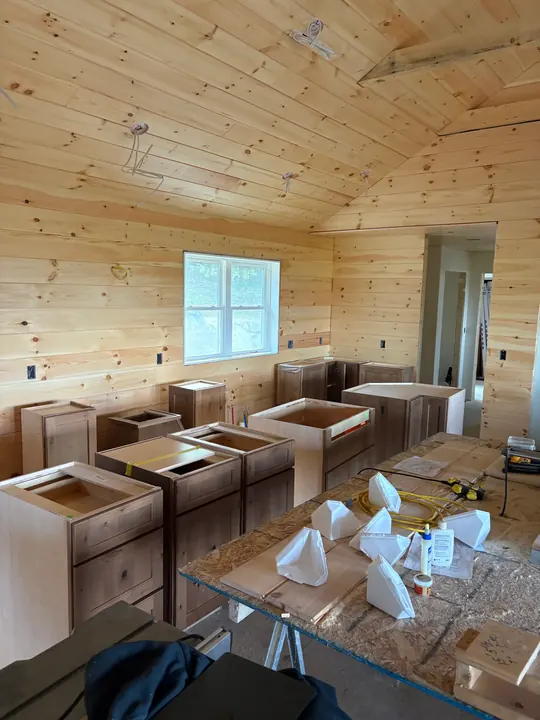 Unassembled cabinet boxes sitting on the floor of a pine-paneled room