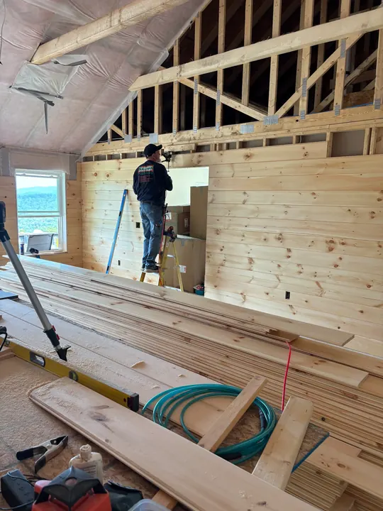 Carpenter on staging putting up pine boards toward a framed gable