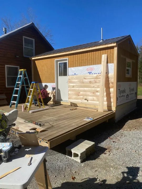 New log-style siding being installed over house wrap on the same shed
